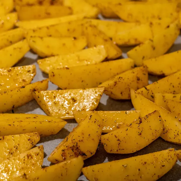 Seasoned potato wedges spread on a tray, ready for baking, showcasing the perfect seasoning process.
